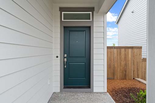A dark teal door with a silver handle is set in a white siding wall.