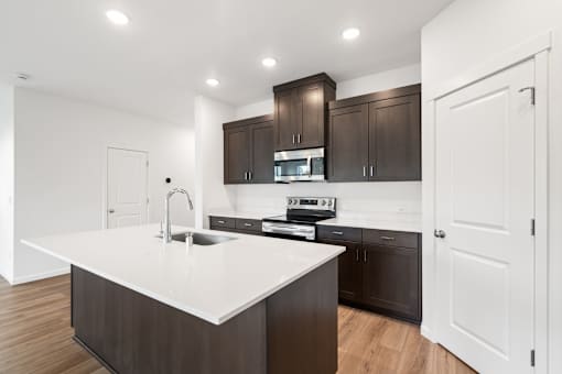 A modern kitchen with dark brown cabinets and white countertops.