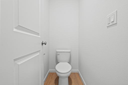 A white toilet in a small bathroom with a door on the left.