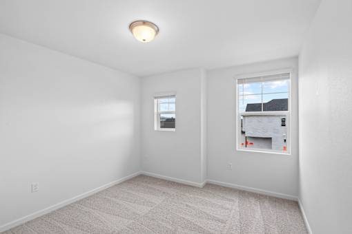 A room with a carpeted floor and two windows.