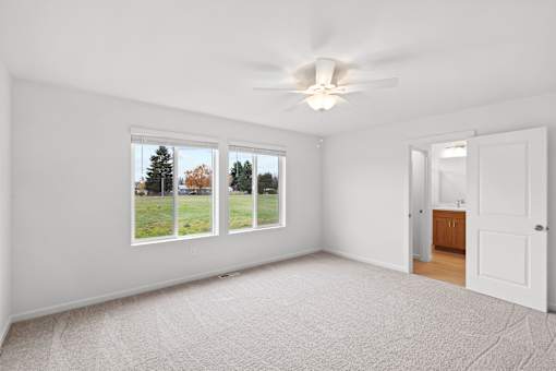 A room with a carpeted floor, a ceiling fan, and a view of trees through the windows.