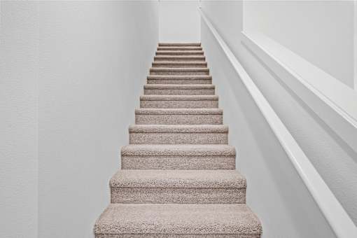 A staircase with beige carpeted steps and white walls.