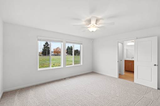 A room with a ceiling fan and a view of trees through the windows.