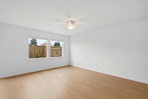A room with a ceiling fan and a window overlooking a fence.