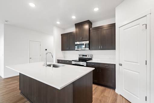 A modern kitchen with dark brown cabinets and white countertops.