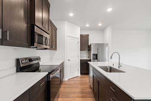 A modern kitchen with dark brown cabinets and white countertops.