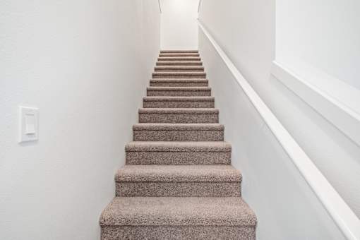 A staircase with a beige carpeted runner and white walls.