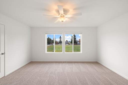A room with a ceiling fan and a window showing a view of trees and a house.