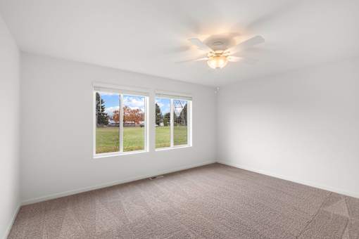 Room with a carpeted floor and a ceiling fan with a window showing a view of trees and a house.
