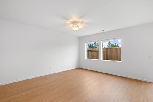 A room with wooden flooring and a window overlooking a fence.