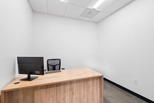A black monitor and laptop on a wooden desk in a white room.
