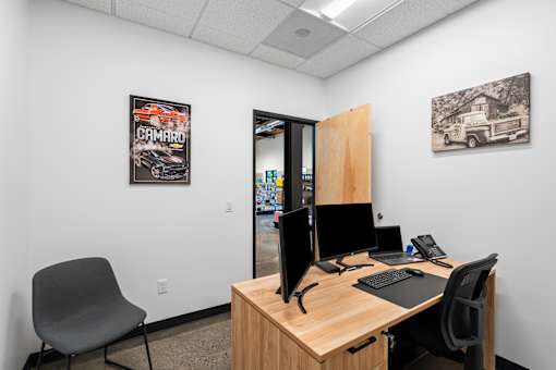 A room with a desk, chair, and two monitors.