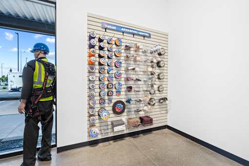 A man in a safety vest and hard hat stands in front of a wall of circular objects.