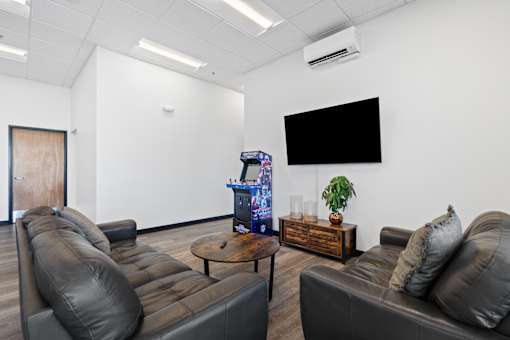 A living room with a brown leather couch, a coffee table, and a flat screen TV mounted on the wall.