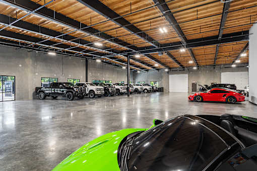 A green car is in the foreground of a large garage with multiple cars.