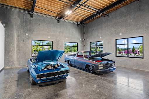 Two cars with their hoods open in a garage.