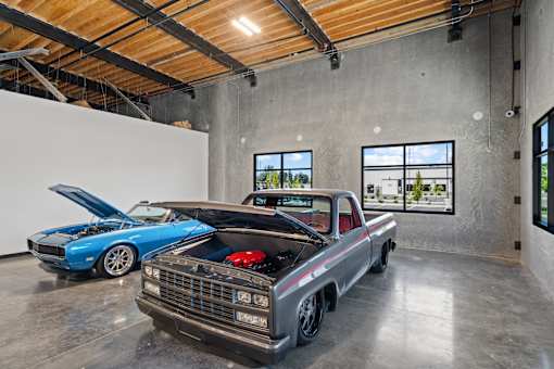 Two cars are parked in a garage with their hoods open.