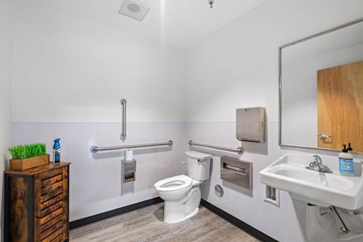 A white toilet with a silver flush handle is in a bathroom with a white sink and a mirror.