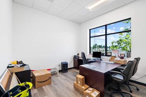 A room with a desk, chairs, and boxes on the floor.