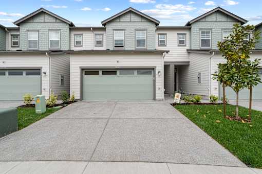 A grey two-story house with a garage door and a tree in front.