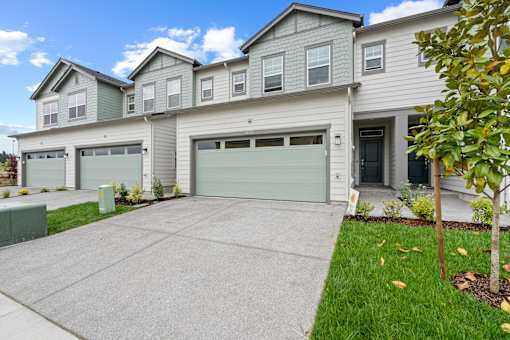 A grey house with a green trash bin in front of it.
