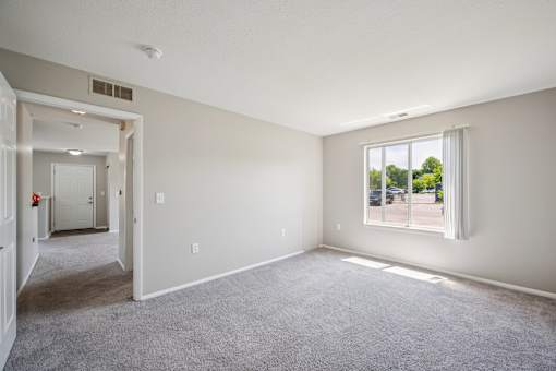 A room with a carpeted floor and a window showing a parking lot outside.