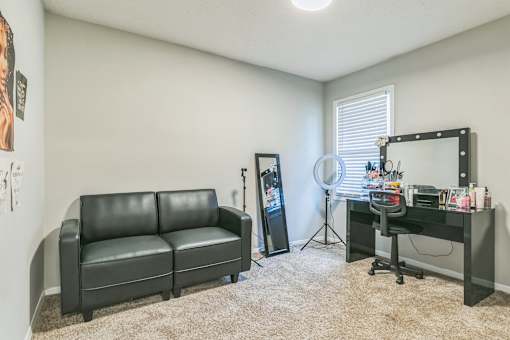 A black leather couch sits in a room with a desk and a mirror.