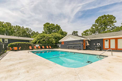 A large outdoor swimming pool surrounded by orange chairs and trees.