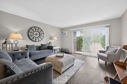 Living room at Renaissance at Carol Stream featuring grey couches and a large wall clock in Carol Stream, IL.
