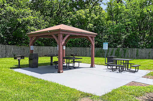 A gazebo with picnic tables is surrounded by a fence and trees.