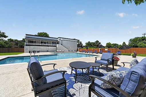 Poolside seating area at Renaissance at Carol Stream featuring blue chairs and a table in Carol Stream, IL.