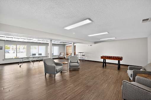 A room with wooden floors and white walls has a piano and several chairs.