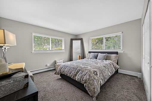 Bedroom at Renaissance at Carol Stream featuring a bed, nightstand, and window with blinds in Carol Stream, IL.