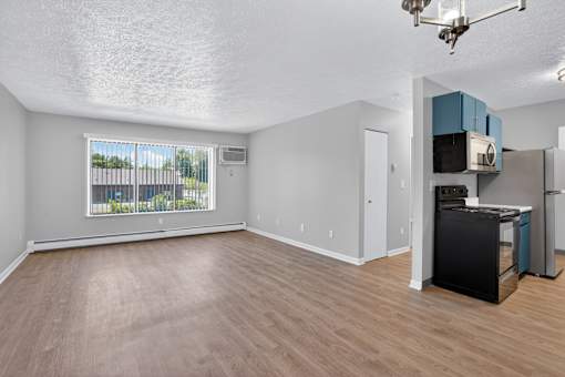 A kitchen area with a black fridge and a window with a view of a fence and trees.