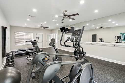 A spacious gym with treadmills, elliptical machines, and a mirrored wall.
