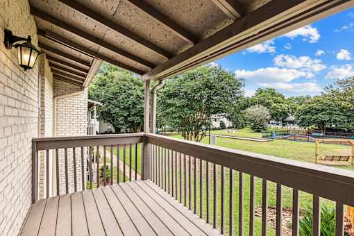 A wooden deck with a railing and a lamp on the wall.