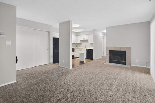A living room with a fireplace and a kitchen in the background.
