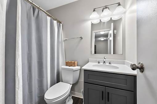 Bathroom at Renaissance at Carol Stream featuring a white toilet, white sink, and grey shower curtain in Carol Stream, IL.