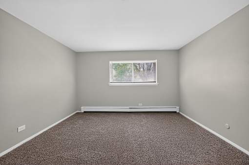 Open bedroom at Renaissance at Carol Stream featuring a window and carpeted floor in Carol Stream, IL.