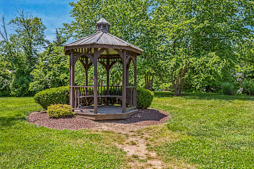 A gazebo is surrounded by a grassy area and trees.