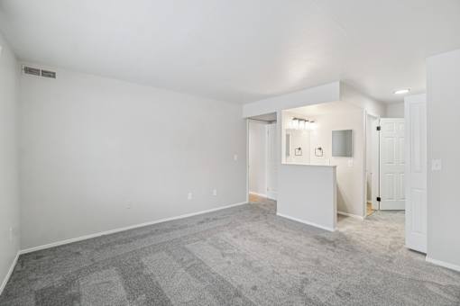 A large empty room with a carpeted floor and a mirrored wall.