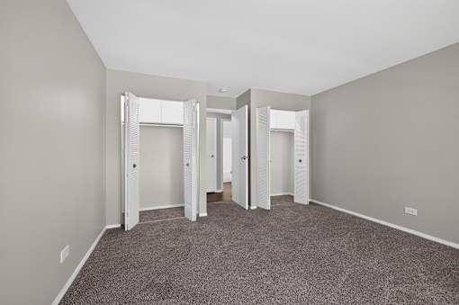 Bedroom at Renaissance at Carol Stream featuring carpeted floor, white walls, and a large closet in Carol Stream, IL.