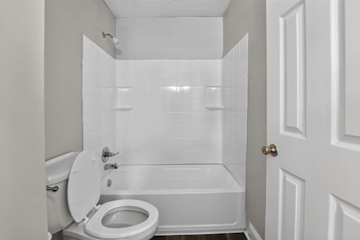 A white bathroom with a toilet, tub, and door.