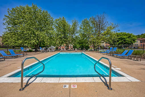 A swimming pool surrounded by trees and lounge chairs.