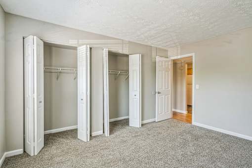 A room with white walls and a carpeted floor with four open closets.
