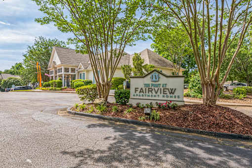 A sign for Fairview Apartment Homes is in the foreground of a parking lot.