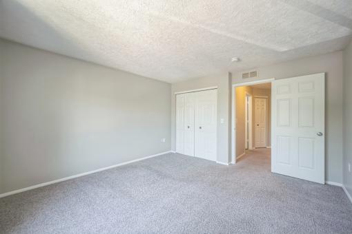 A room with white walls and carpeted floor with two doors.