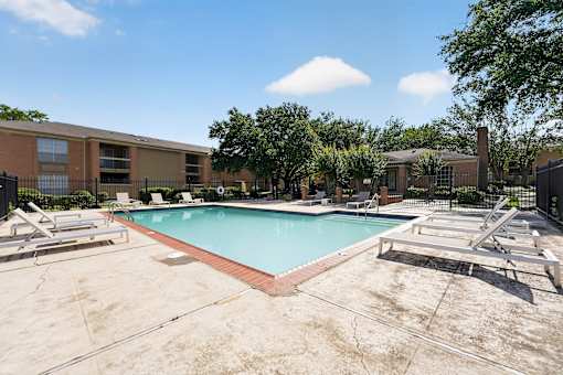 A swimming pool surrounded by a concrete floor and lounge chairs.