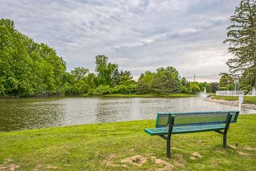 A green bench is situated on the grass by a body of water.
