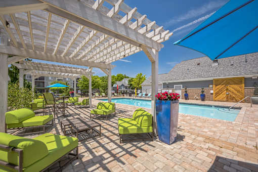 A poolside area with green lounge chairs and a white pergola.